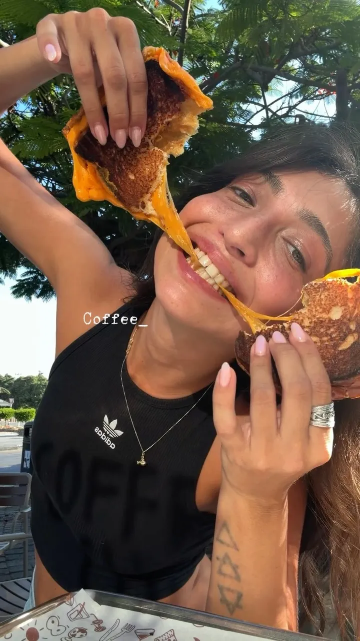 לקוחה מחייכת מותחת גריל צ'יז נמס לשניים מול העדשה, בשמש של אשקלון